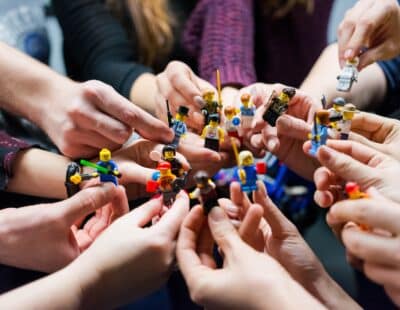 Haende halten diverse Legofiguren in die Mitte