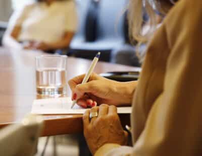 Bild mit zwei einander gegenüber sitzenden Personen. Eine davon ist am Schreiben.