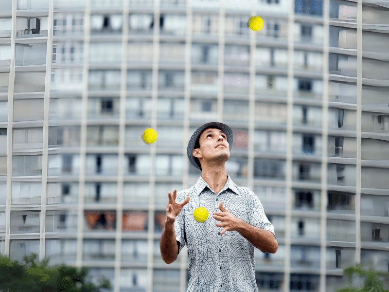 Mann jongliert konzentriert Bälle vor einem Bürogebäude